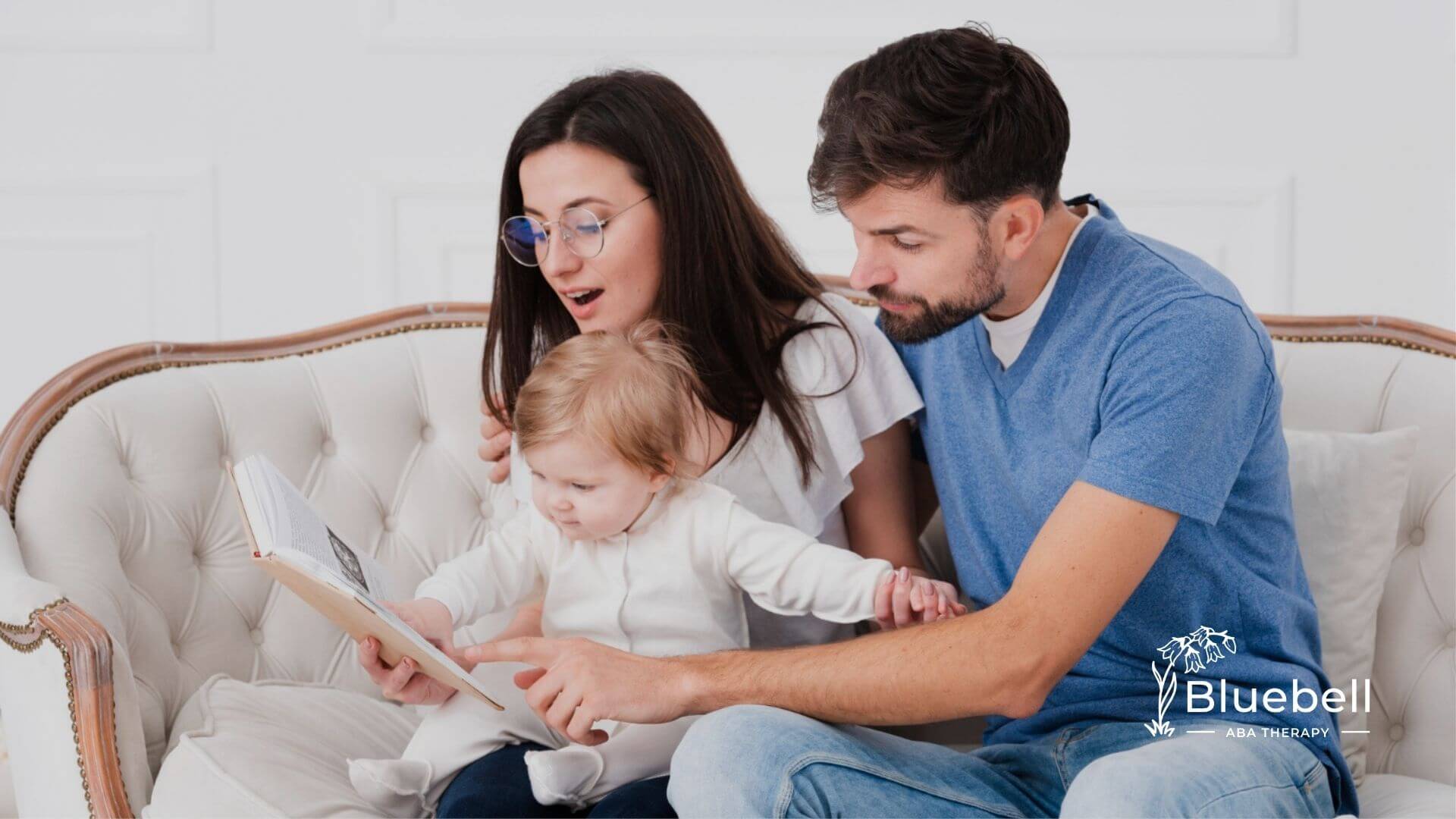 Parents reading a book together with their baby on a couch during in-home ABA.