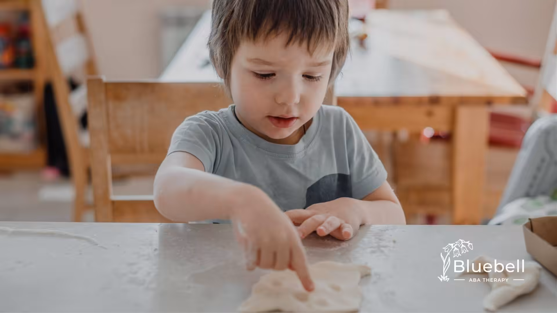 Young child with autism pressing a finger into flattened dough at a table in ABA therapy.