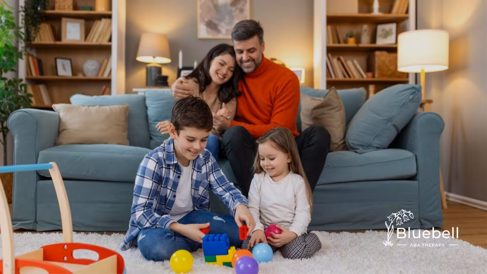 Parents sitting on a couch while two young children with autism play together on the floor at home.