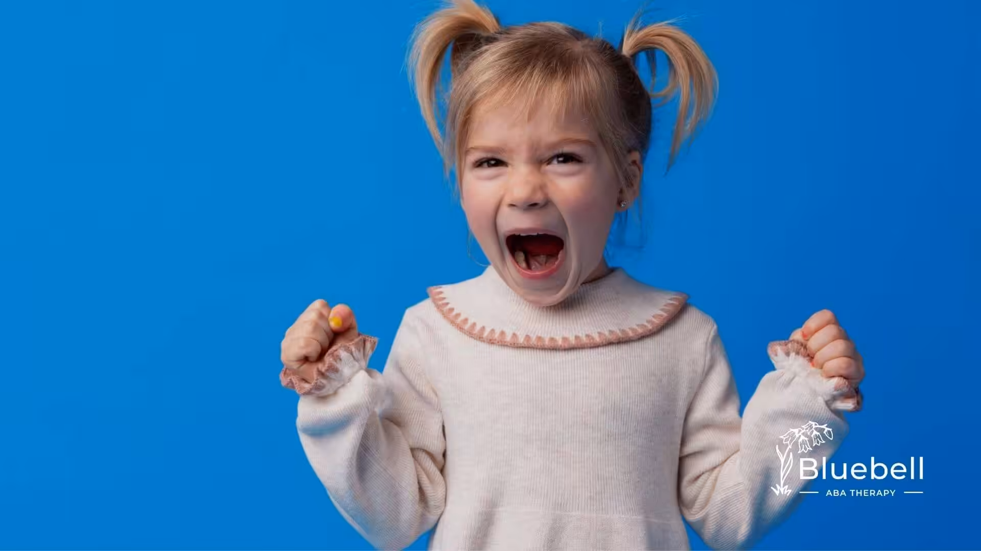 Young girl with pigtails shouting angrily in ABA therapy, fists raised against a blue background.