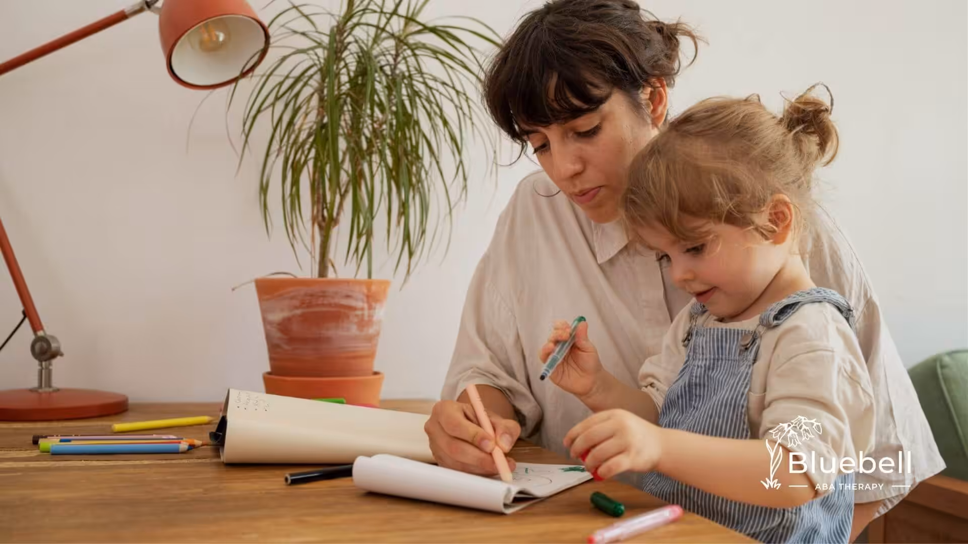 BCBA and toddler drawing together at table during ABA therapy.