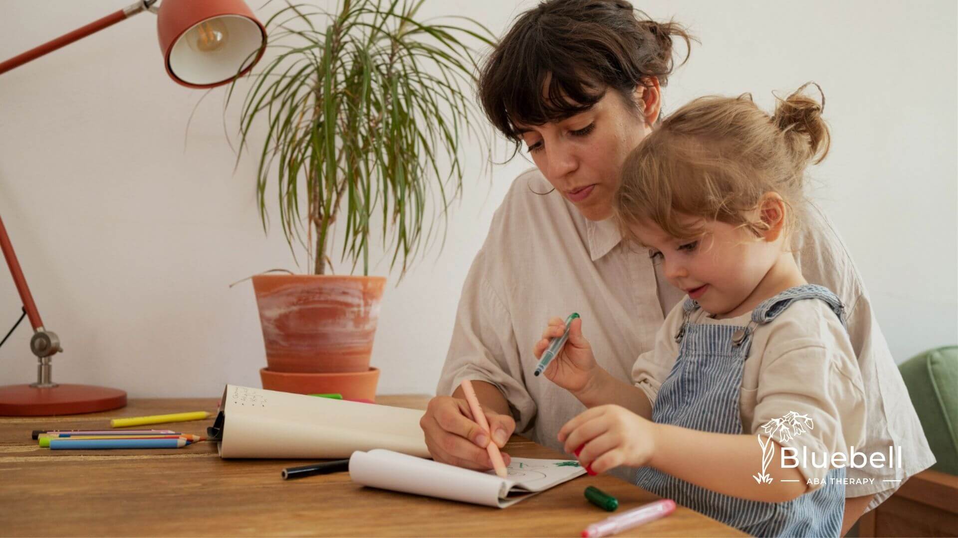 BCBA and toddler drawing together at table during ABA therapy.