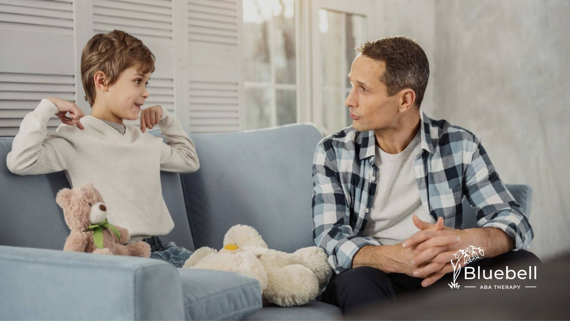 BCBA sitting on a couch talking seriously with a young boy during ABA therapy.
