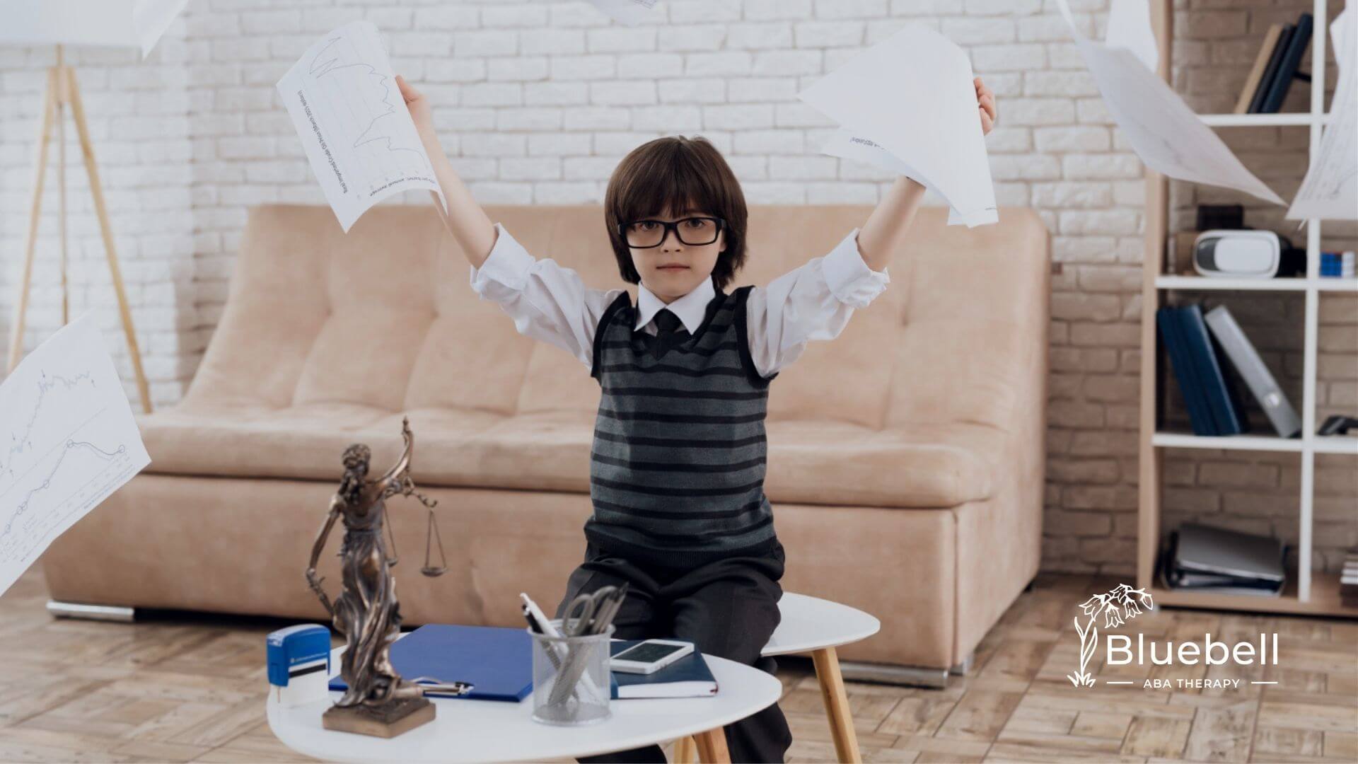 Young boy in glasses holding papers at desk during ABA therapy.