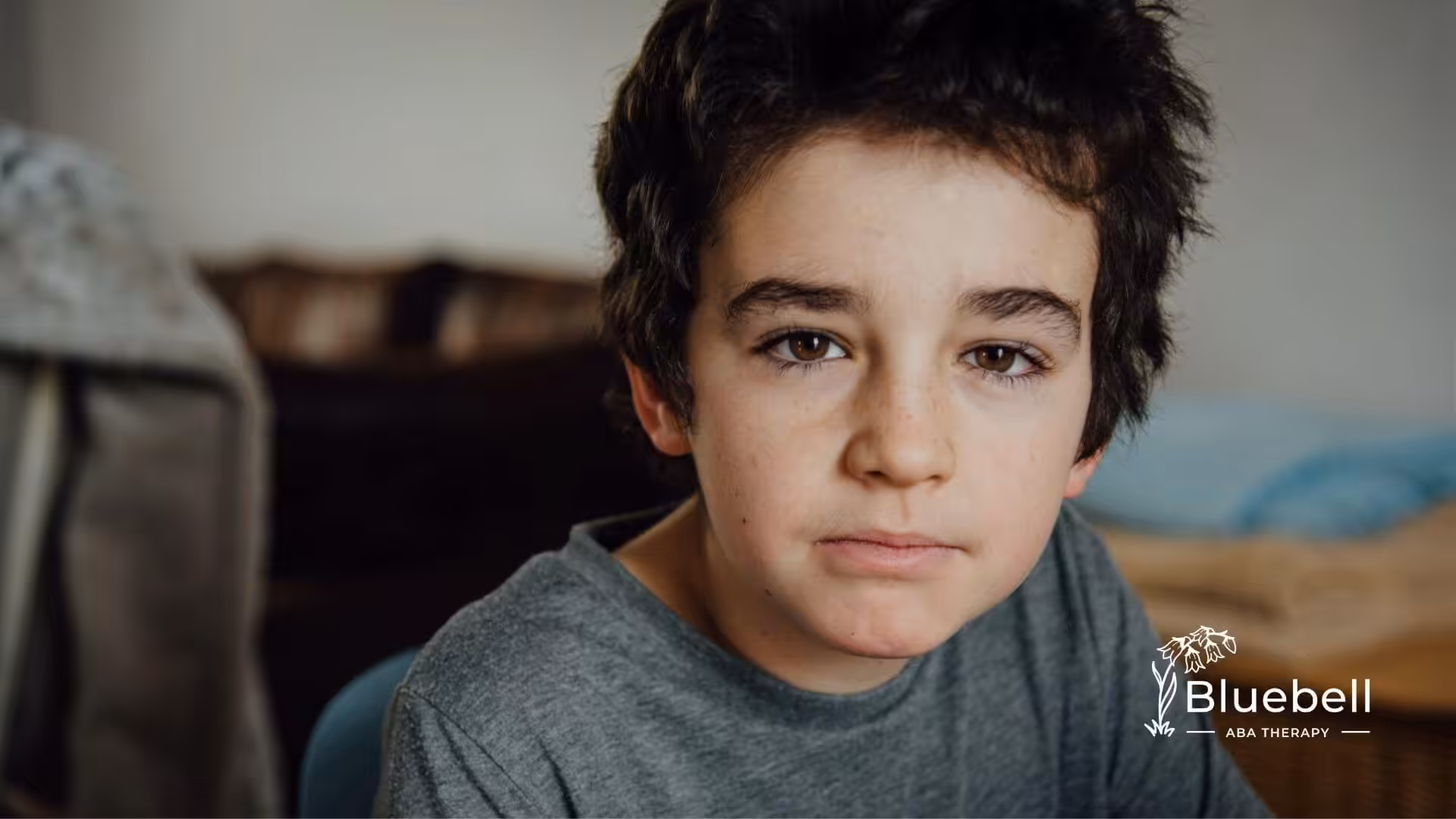Close-up of a child with short dark hair looking calmly at the camera indoors during ABA therapy.