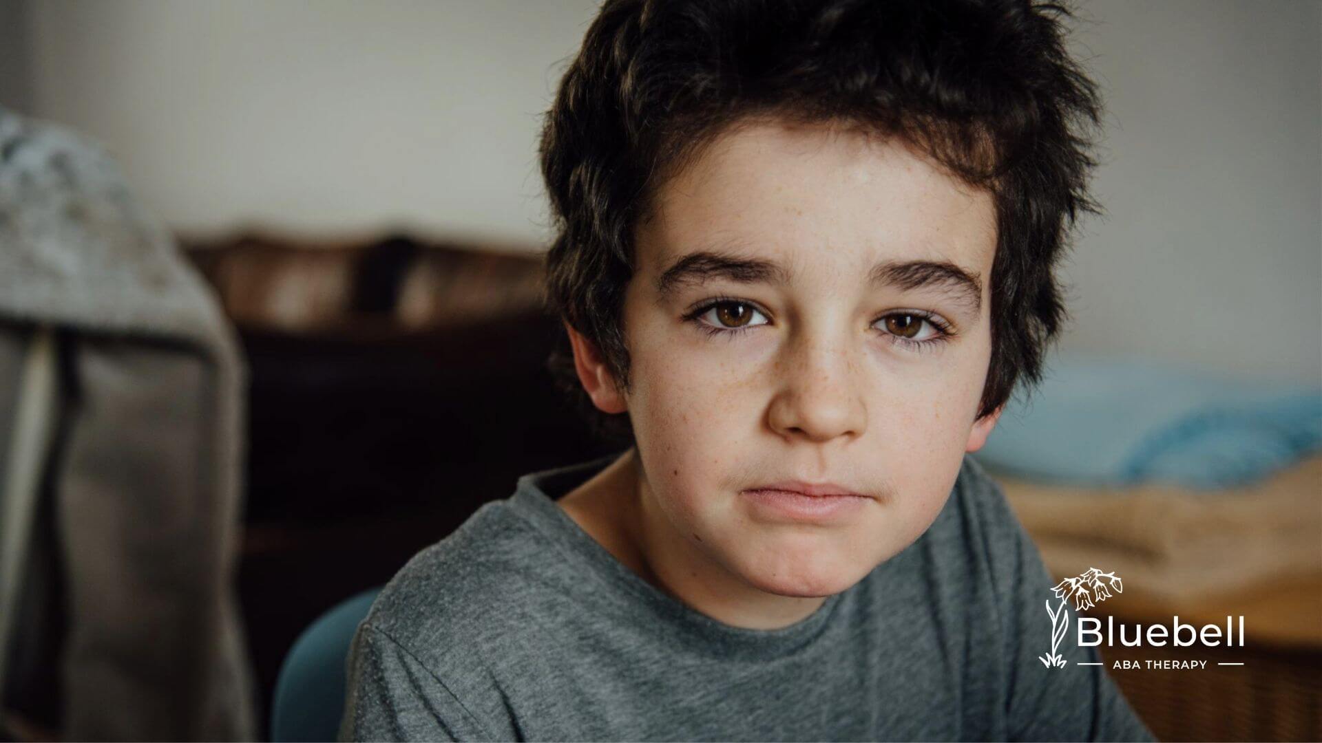 Close-up of a child with short dark hair looking calmly at the camera indoors during ABA therapy.