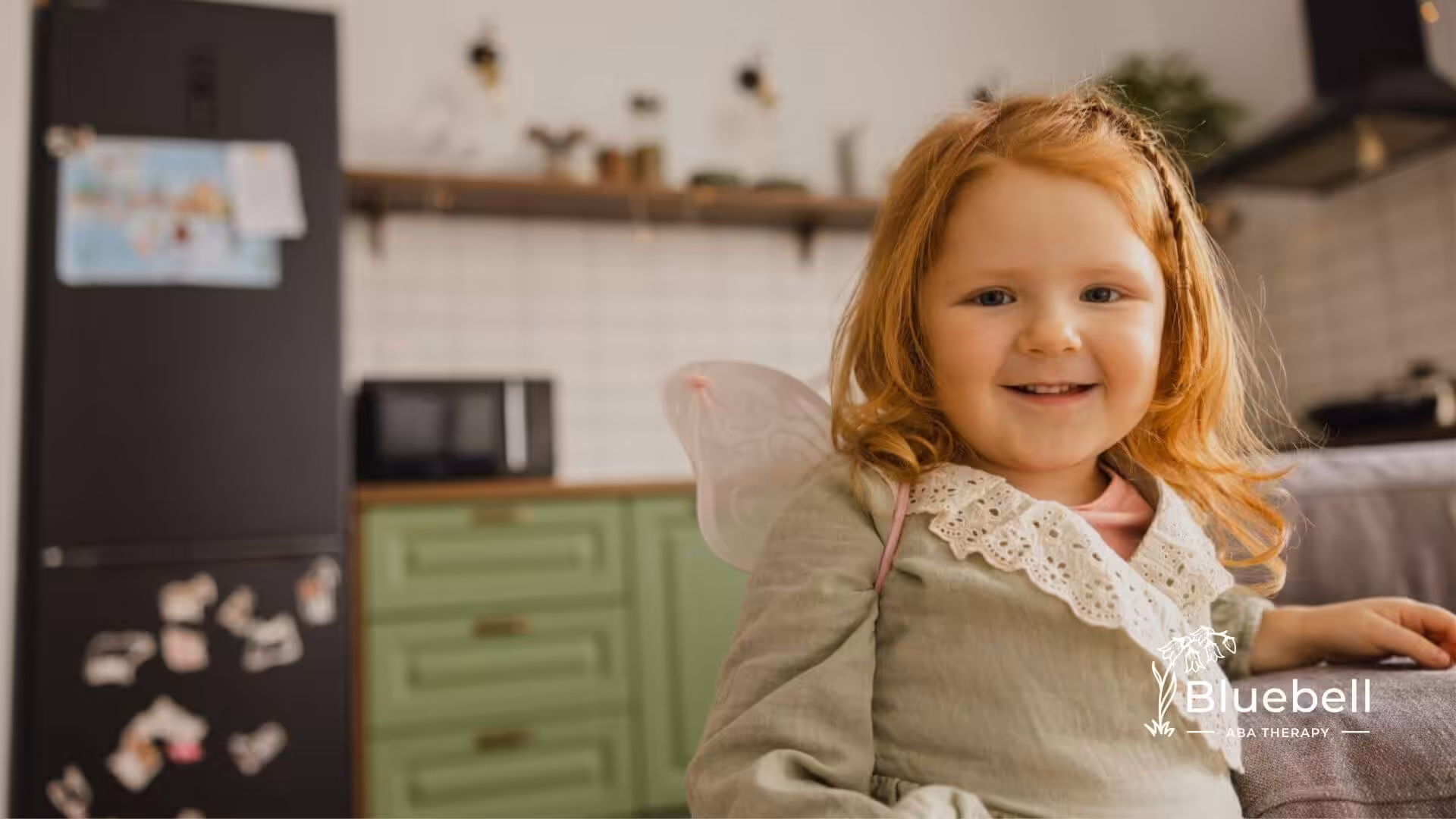 A smiling young child with red hair wearing small fairy wings in ABA therapy.