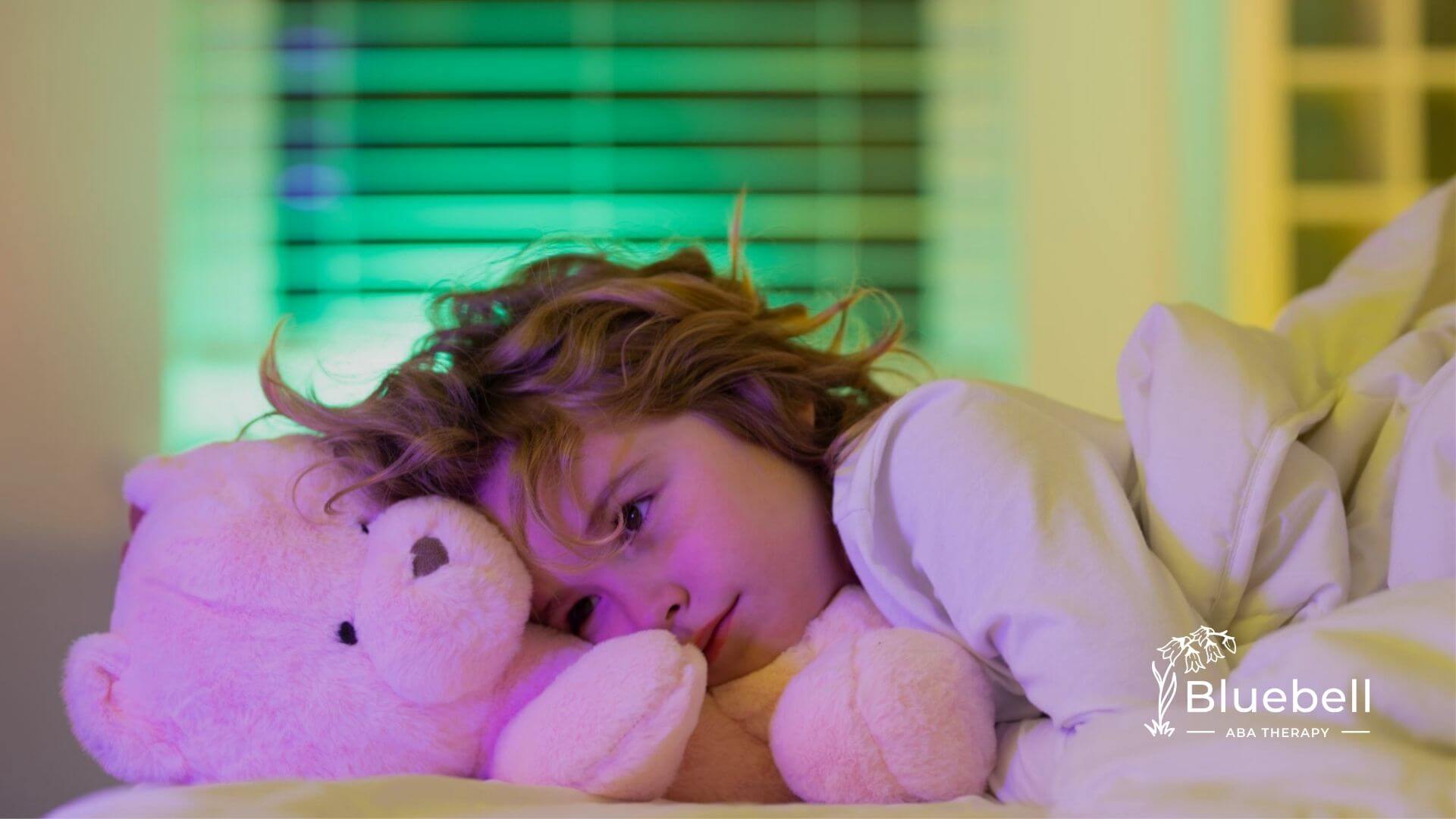 Child with autism lying in bed holding stuffed teddy bear.